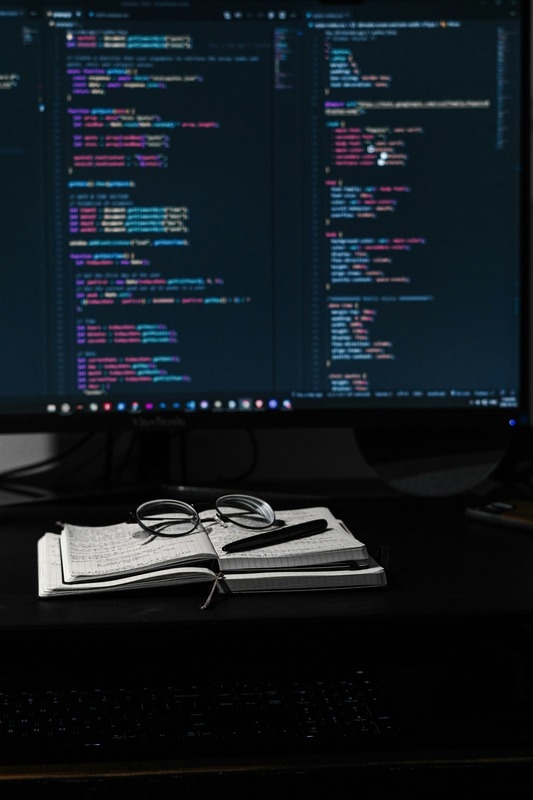 A desk of a developer with display, notebook and eye glasses.